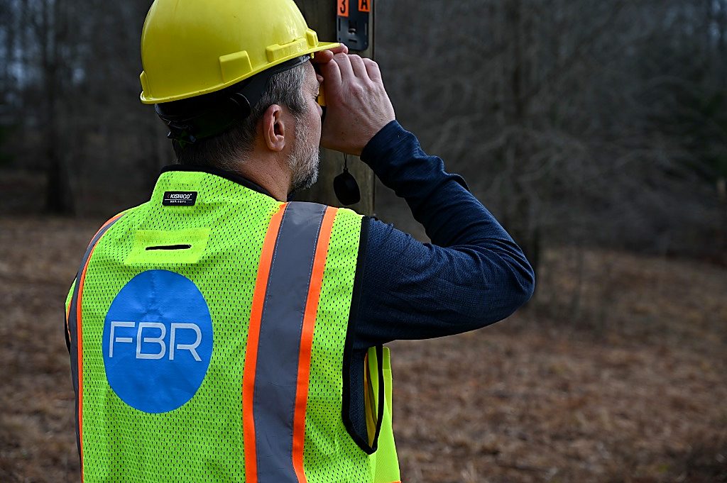 Field crew in FBR safety vest inspecting a utility pole.